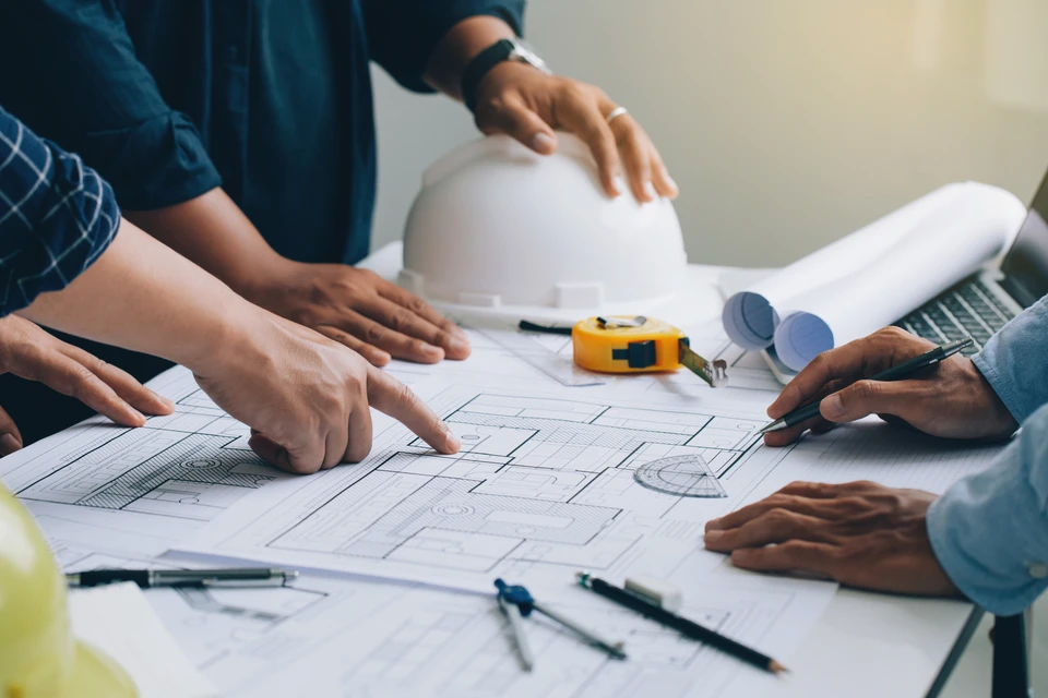 Deux hommes en tenue professionnelle analysent des plans d'architecture sur une table blanche dans un bureau moderne